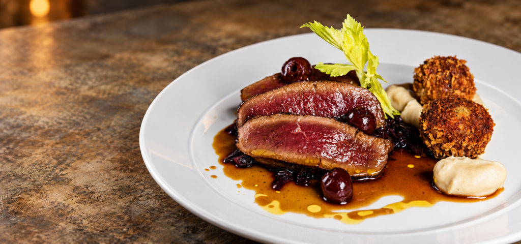 Sliced meat served with vegetables, golden croquettes and sauce on a white plate at The Butchers Arms.